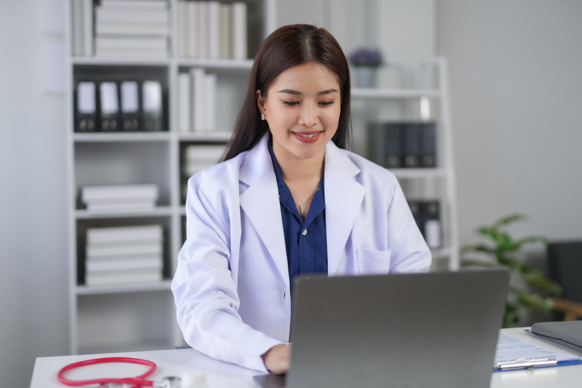 Young female doctor in white coat using laptop in modern medical office